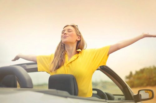A cheerful woman in a yellow shirt enjoys freedom on a sunny drive in a convertible.